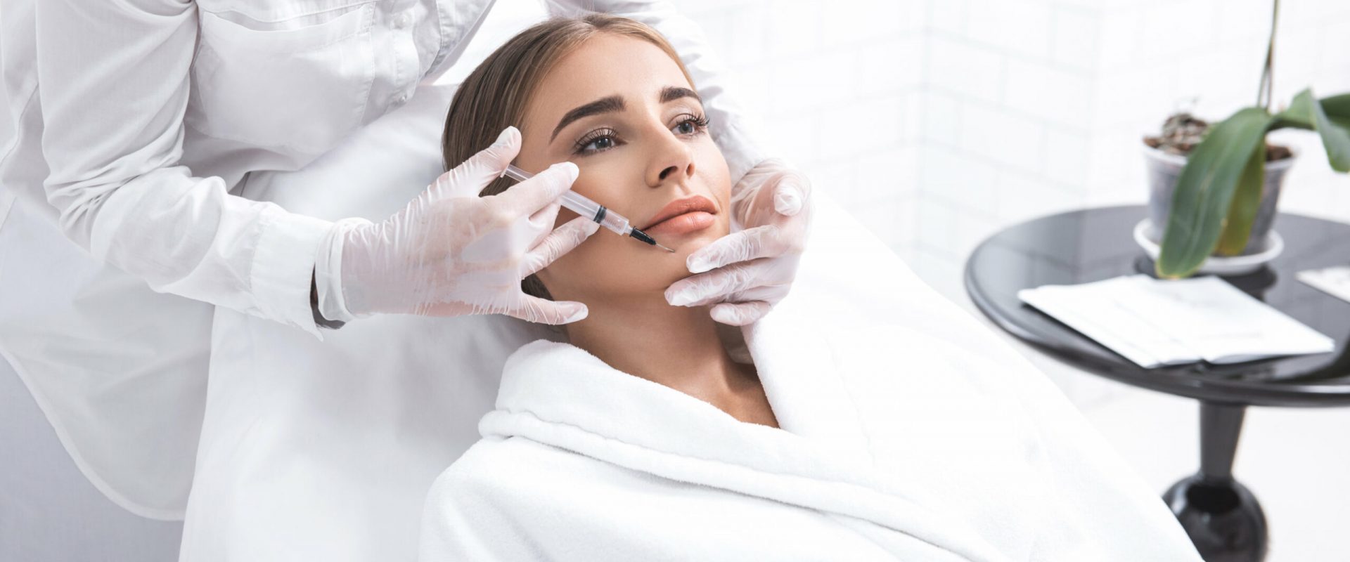 Beauty procedure. Female beautician making injection to girl chin. She is wearing sterile gloves and using syringe