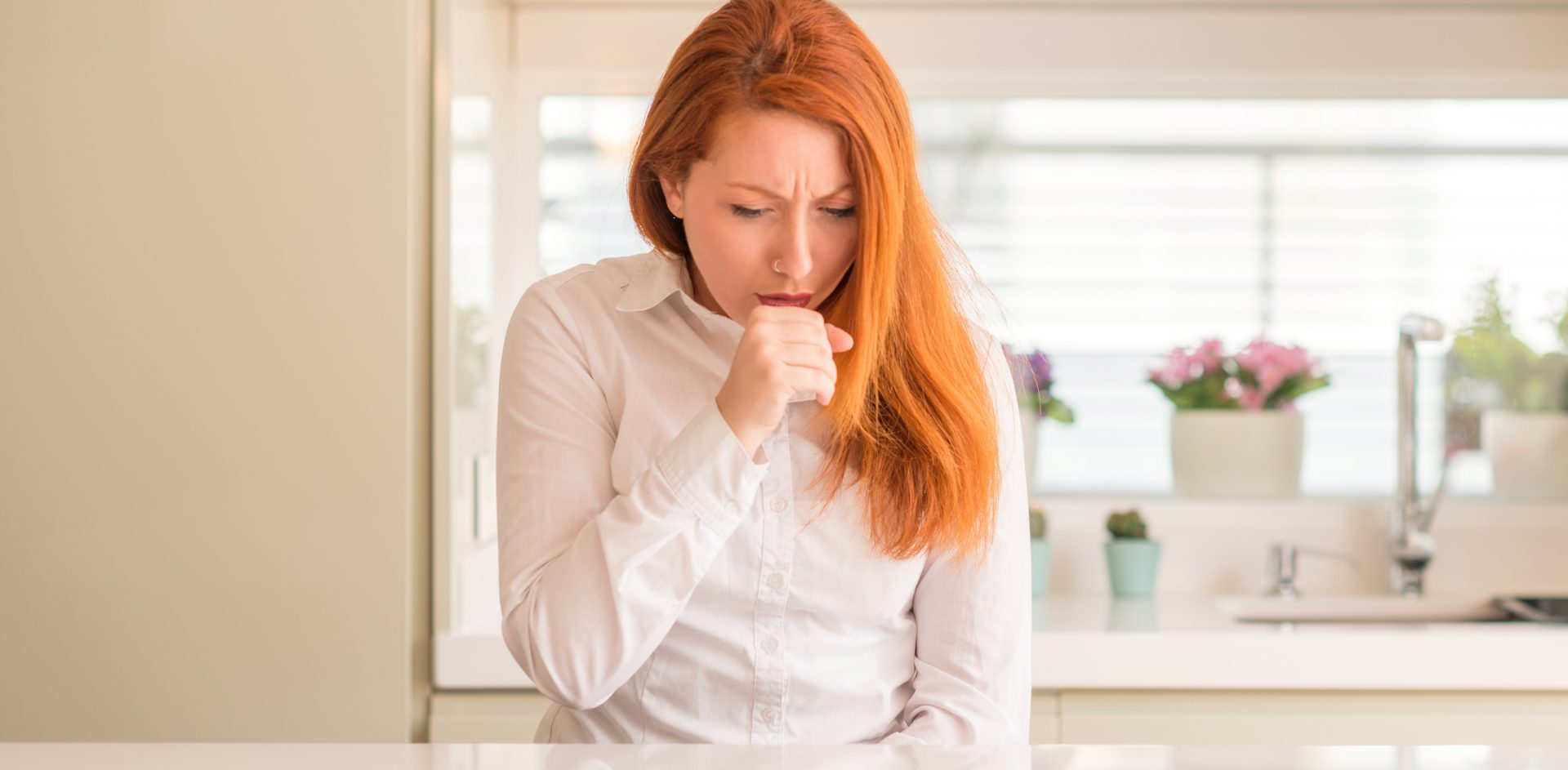 Redhead woman at kitchen feeling unwell and coughing as symptom for cold or bronchitis. Healthcare concept.