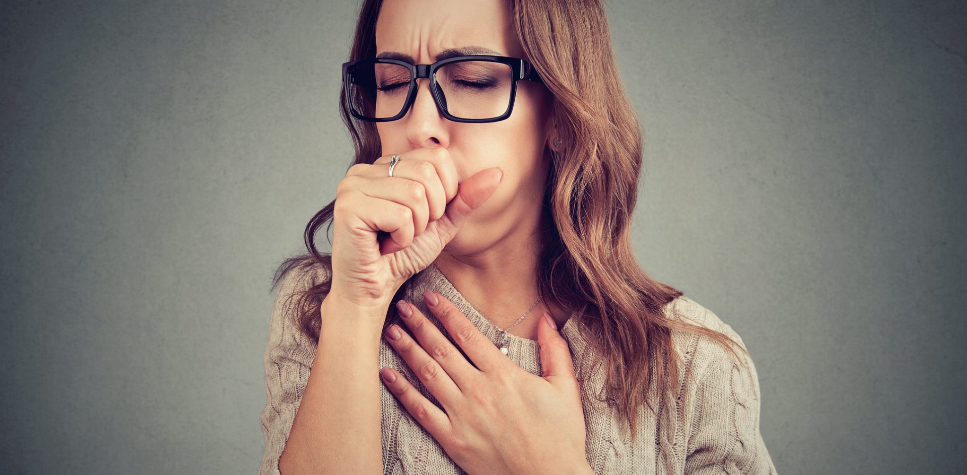 Young woman having asthma problems and coughing badly covering mouth and holding hand on chest.